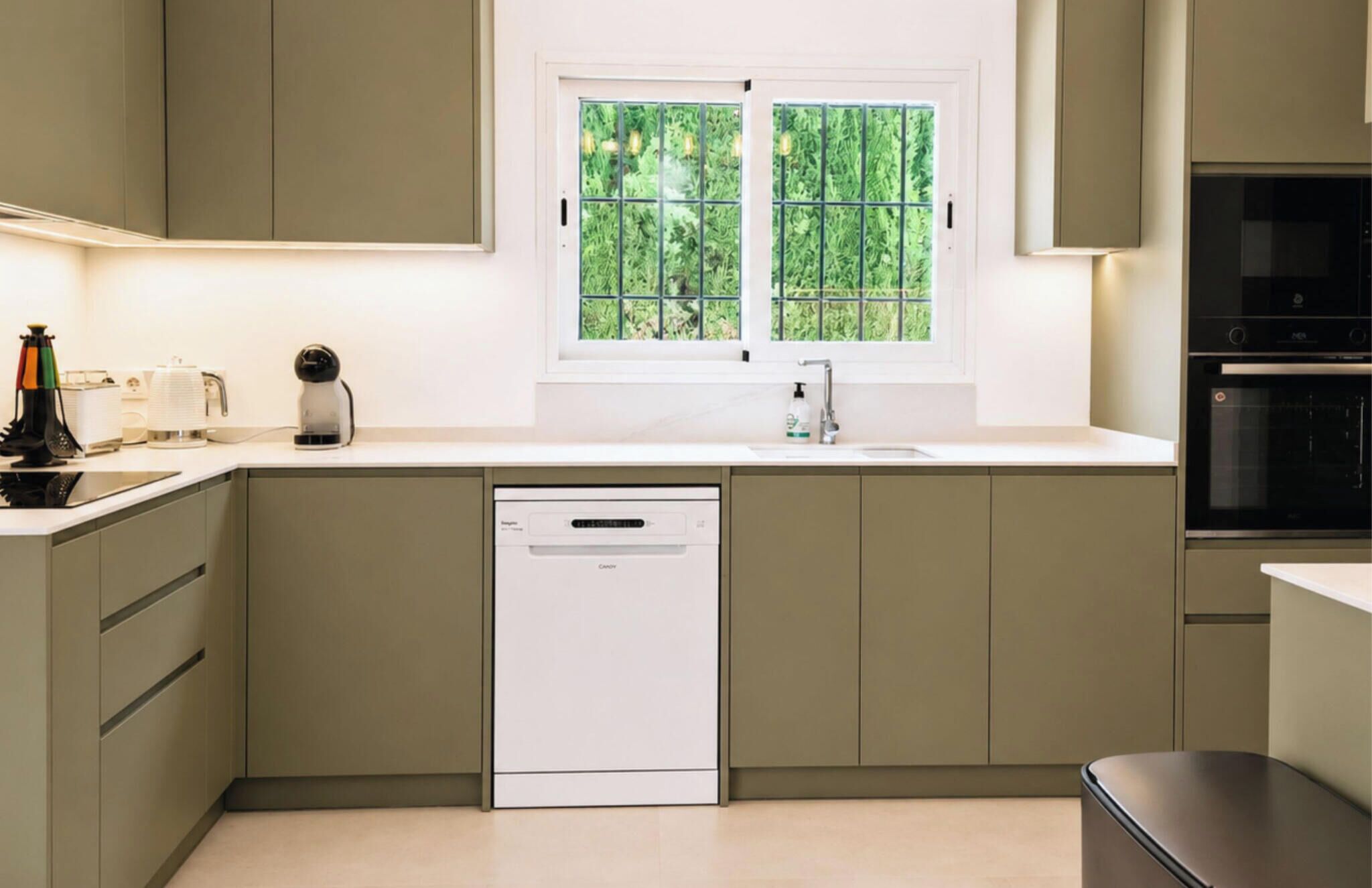 Een keuken met een vaatwasser, een spoelbak en een raam met uitzicht op groen.