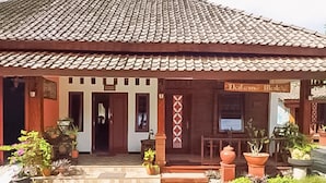 A building with a tiled roof, a sign reading 'Deli & Cafe,' and a front porch with potted plants. - Borobudur Daleme Make Homestay (Borobudur)