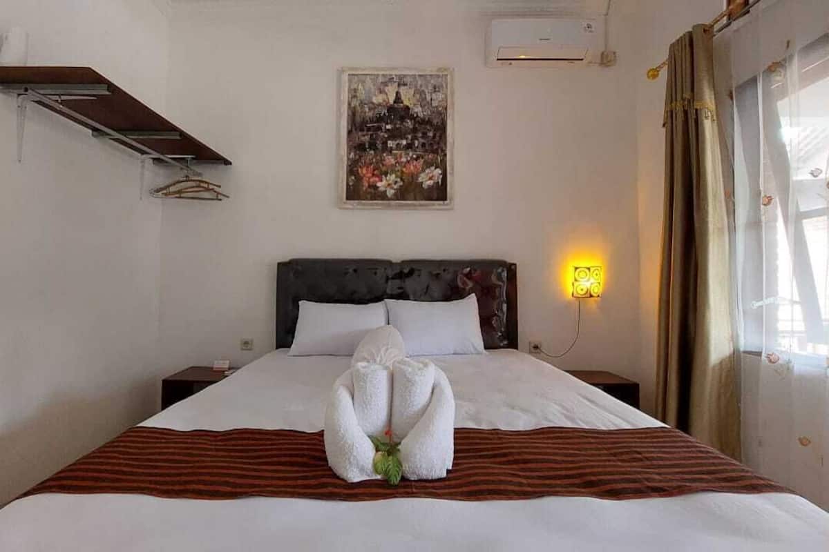 Une chambre d’hôtel avec un lit, une étagère fixée au mur, un tableau et une fenêtre avec des rideaux.