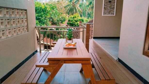A wooden table with a tray and a potted plant on a balcony with a view of greenery. - Borobudur Daleme Make Homestay (Borobudur)