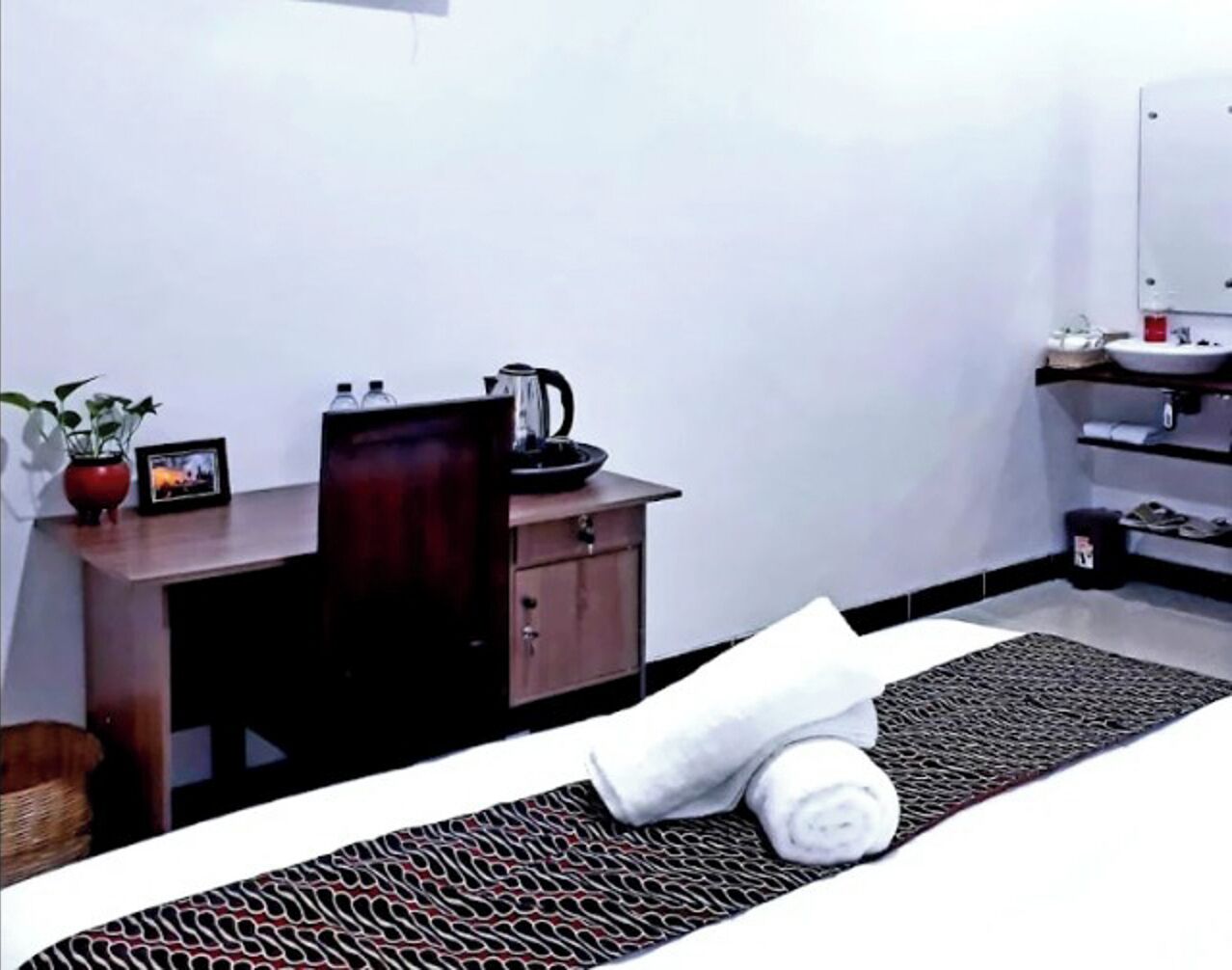 Ein Hotelzimmer mit Bett, Schreibtisch, Kaffeemaschine, kleiner Ablagefläche, Pflanze und Spiegel.