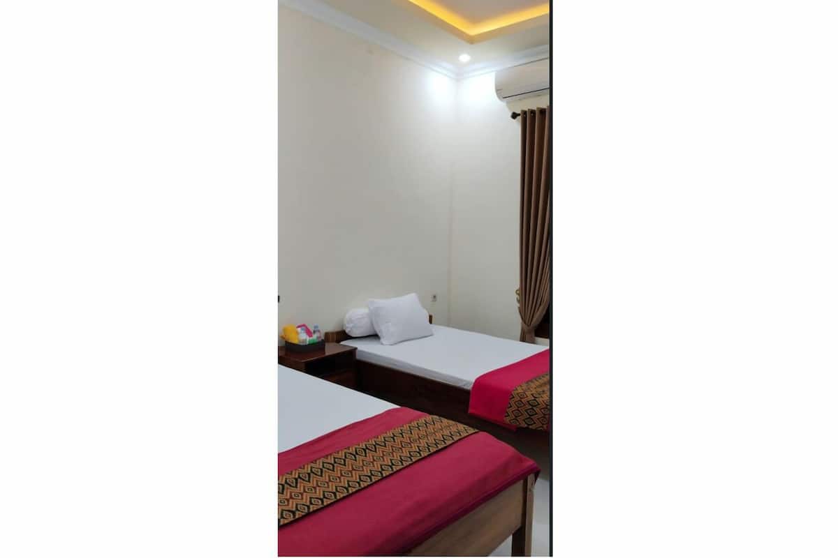 Une chambre d’hôtel avec deux lits, une table de chevet, un climatiseur fixé au mur et un luminaire au plafond.