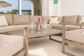 A modern outdoor seating area with a cushioned sofa and a table, a bottle of champagne, and two glasses. - Villa La Colina by Interhome (Moraira)