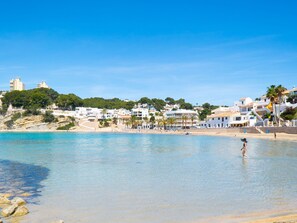 Eine Küstenstadt mit Häusern entlang des Strandes, klarem blauen Wasser und einer Person, die im Wasser steht.
