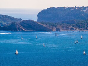 A coastal scene with multiple sailboats on the water, surrounded by rocky cliffs and a distant town. - Villa Bonita by Interhome (Moraira)