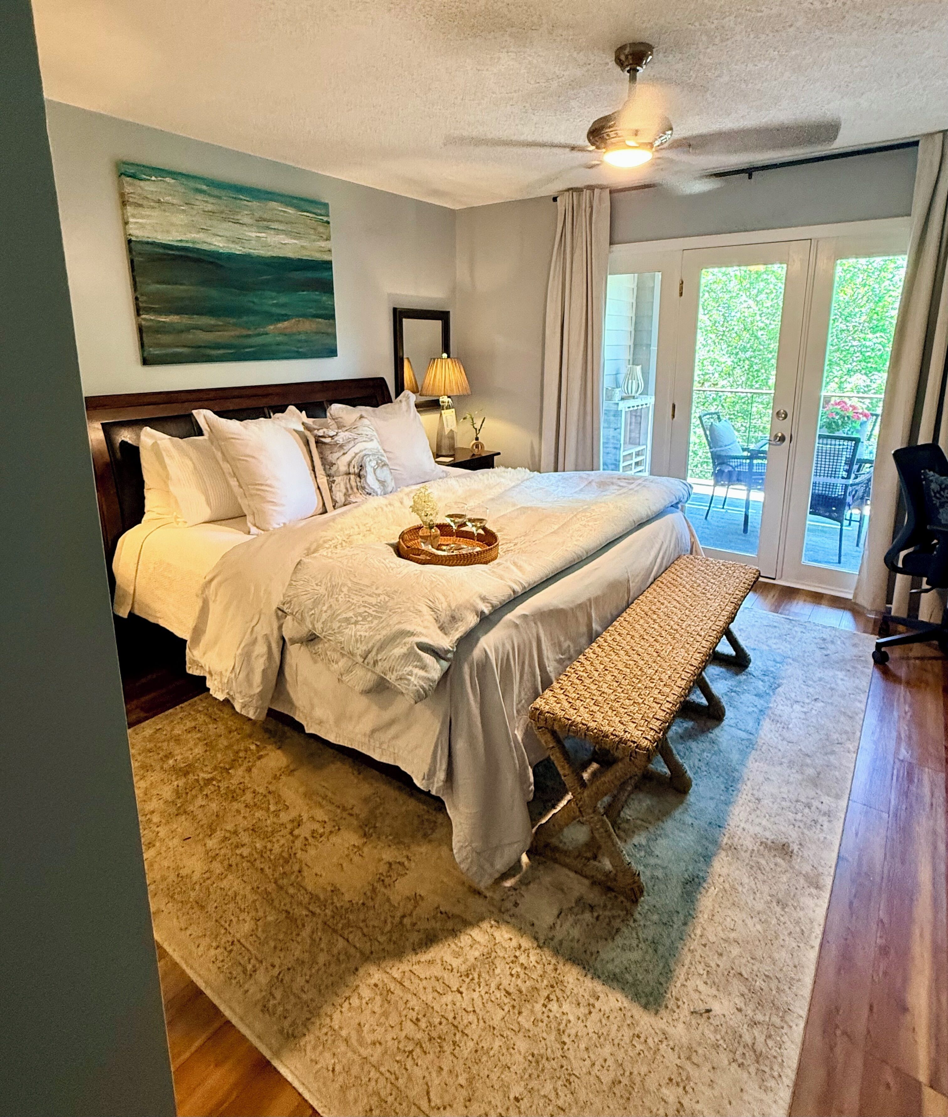 A bedroom with a bed, bedside table, lamp, and a view of the outdoors.