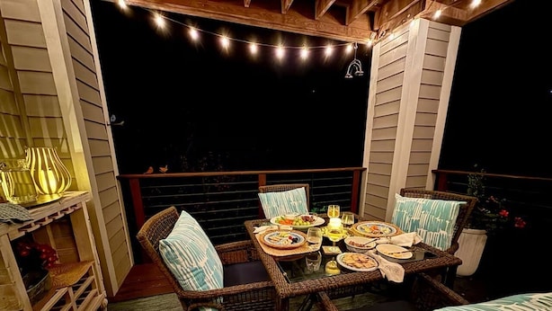 An outdoor dining area with wicker furniture, string lights, and a table set for a meal. - Designer Boutique Retreat • 2 Private King Suites • Fireplace • View ... (Banner Elk)
