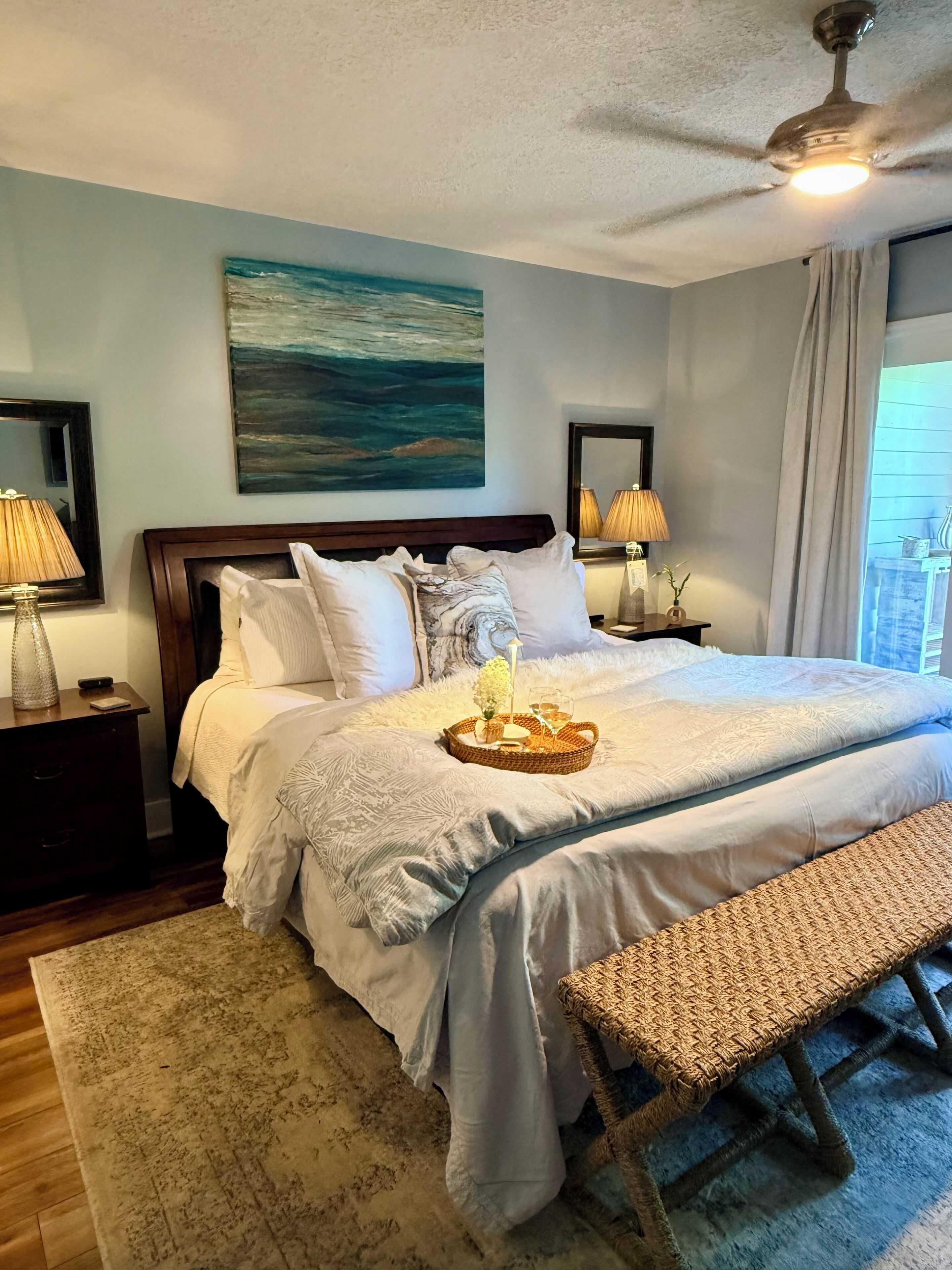 A neatly made bed with a tray of items, a wooden headboard, and a ceiling fan.