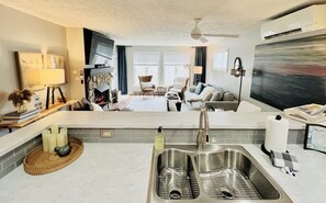 A modern kitchen with a double sink, a dining area with a sofa, and a large window.