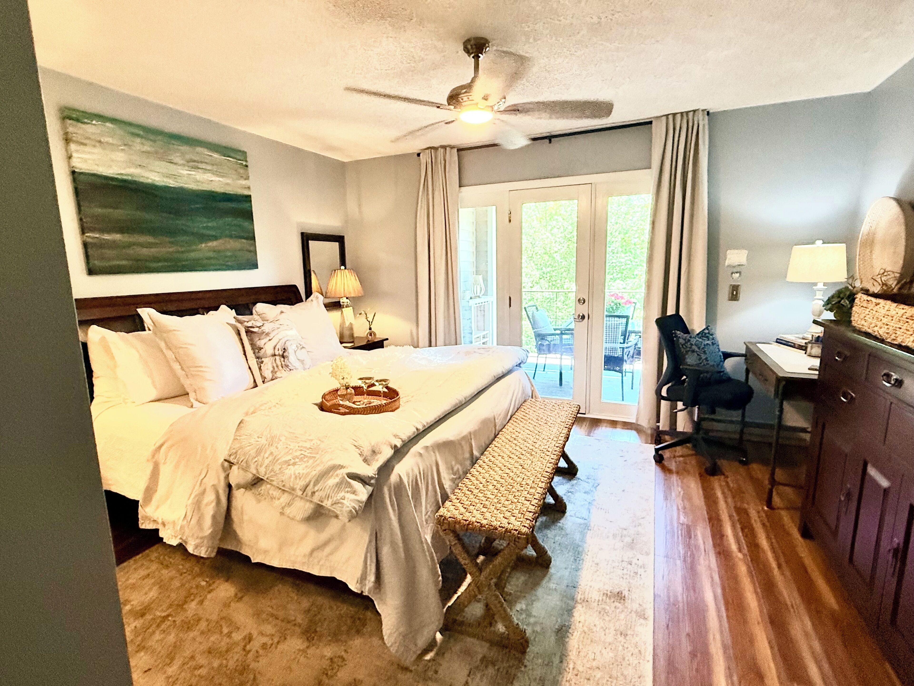 A hotel room with a bed, a desk, a chair, a ceiling fan, and a view through the door.