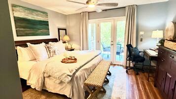 A hotel room with a bed, a desk, a chair, a ceiling fan, and a view through the door.