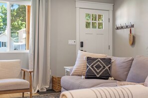 A living room with a sofa, a chair, a door, and a wall-mounted coat rack. - The Perfect CDA Escape - Beach, Trails & Downtown All Within Walking Distance (Coeur d'Alene)