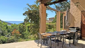 Ett utomhusområde med plats för måltider, med utsikt över havet, en pergola och en grill.