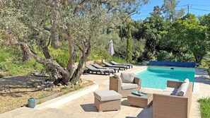 Un espace aménagé au bord de la piscine, avec des chaises longues, une petite table et un plateau, ainsi qu’une piscine.