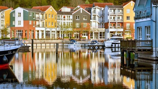 Une rangée de maisons de ville aux couleurs vives longe un canal paisible où sont amarrés des bateaux.