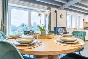 A dining table set with plates, glasses, and cutlery, surrounded by chairs, in a room with large windows and a view of greenery. - Gite - 3 bedrooms - sleeps 6 (ROBELMONT)