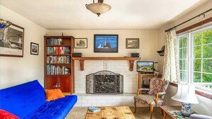 Uma sala de estar com um sofá azul, uma mesa de centro de madeira, uma lareira, uma estante de livros e uma janela com cortinas.