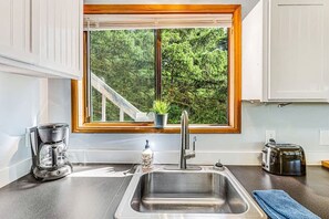 A kitchen with a stainless steel sink, a coffee maker, a toaster, and a window with a view of trees.
