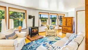 A spacious room with a fireplace, large windows, a sofa, and a wooden cabinet. - 3BR Copalis Beach Cottage | Fireplace | Dogs OK (Copalis Beach)