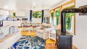 A modern kitchen with white cabinets, a dining area with white chairs, a sofa, and a large window with a view of greenery. - 3BR Copalis Beach Cottage | Fireplace | Dogs OK (Copalis Beach)