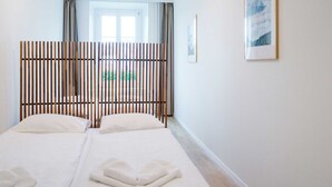 Quarto de hotel com duas camas, janela com cortinas, quadro na parede e vista para o verde lá fora.