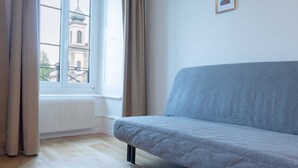 Quarto com uma cama de solteiro, um radiador, uma janela com cortinas e um quadro na parede.