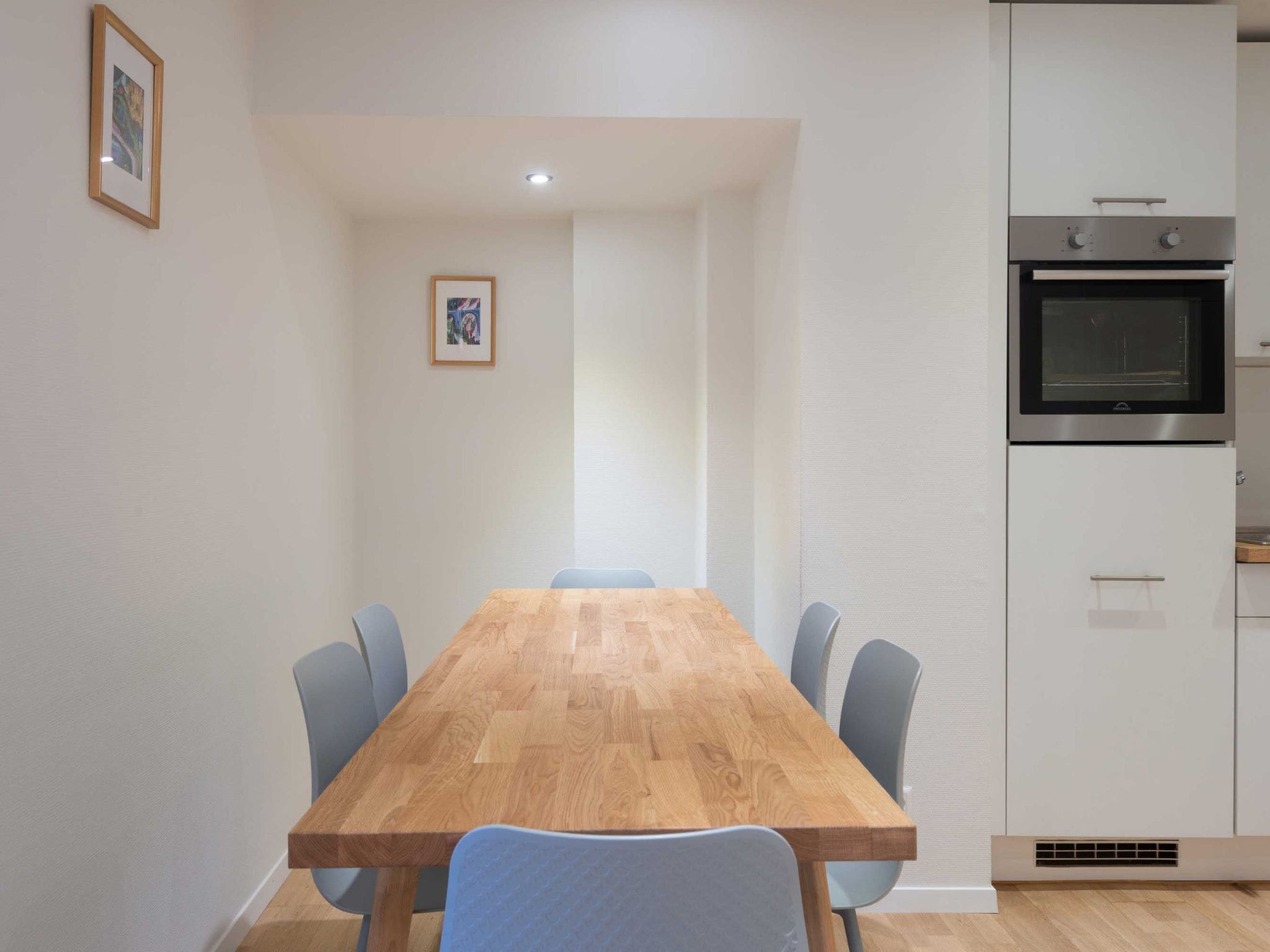 A modern kitchen with a built-in oven and a dining area with a wooden table and chairs.