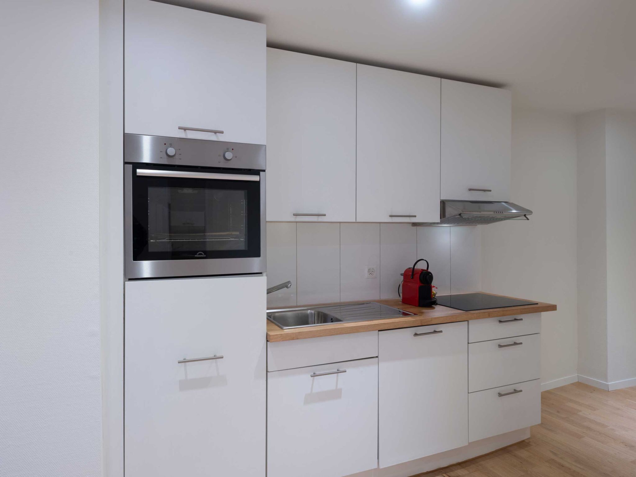 Una cocina moderna con armarios blancos, un horno de acero inoxidable, un lavamanos y un calefactor portátil rojo.
