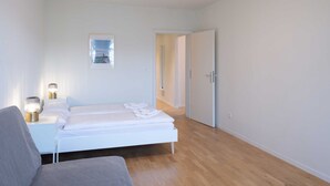 Ein Schlafzimmer mit einem Bett, Nachttischen, einem Sessel, einer Tür und einem Flur.
