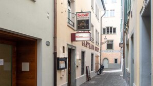 Eine schmale Straße mit Gebäuden an beiden Seiten, darunter ein Restaurant namens 'Schiff' und ein Schild für 'HIT Vermietung'.