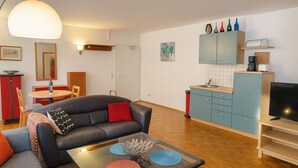 A compact living space with a sofa, coffee table, dining area, kitchenette, and a television.