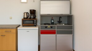 A compact kitchenette with a white refrigerator, a coffee maker, a toaster, a sink, and a small cabinet.