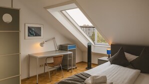 A bedroom with a desk, chair, bed, and a window with a view.