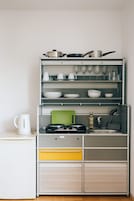 Una cocina con un mueble empotrado, hervidor, tabla de cortar, lavamanos y un esparacimos para copas de vino.