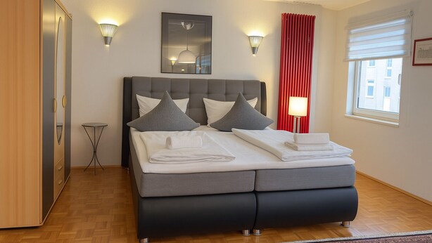 A modern bedroom with a bed, bedside lamps, a red curtain, and a window. - BoardingHouse - Studios & Apartments (Kassel)