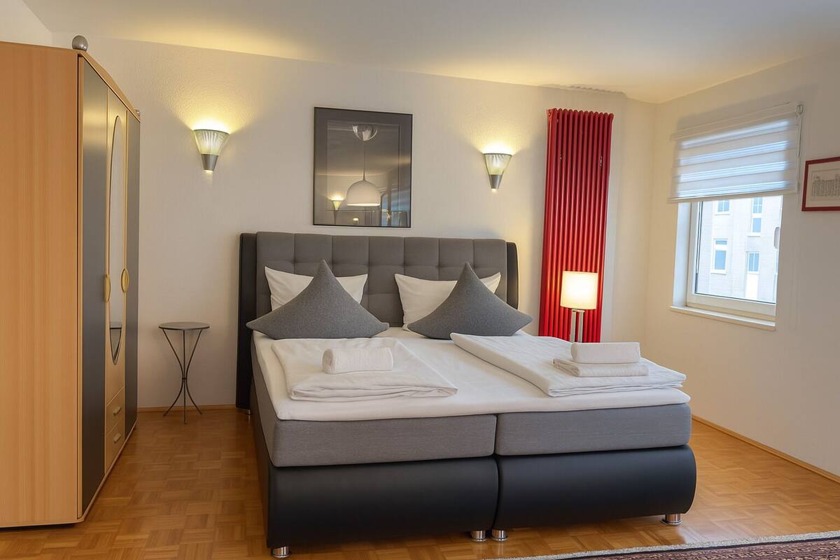 A modern bedroom with a bed, bedside lamps, a red curtain, and a window.