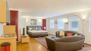 A modern apartment with a kitchenette, a grey sofa, a bed, and a large window. - BoardingHouse - Studios & Apartments (Kassel)
