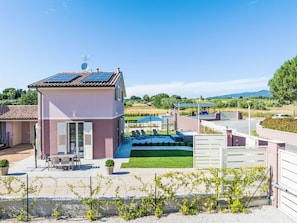 A two-story house with a solar panel roof, a patio with outdoor furniture, and a swimming pool.