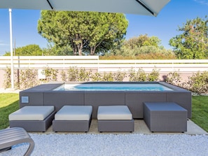 A swimming pool with a pergola overhead, surrounded by outdoor seating and a white fence.