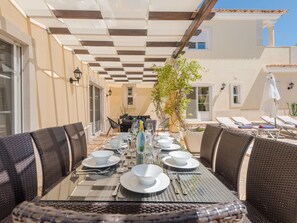 An outdoor dining area with a table set for four, surrounded by wicker chairs, under a pergola with a checkered ceiling. - Endless Summer Luxury Villa by Interhome (Almancil)