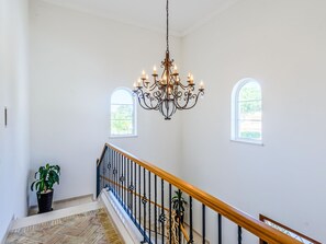 A spacious interior with a grand chandelier, a staircase with a wooden handrail, and two arched windows. - Endless Summer Luxury Villa by Interhome (Almancil)
