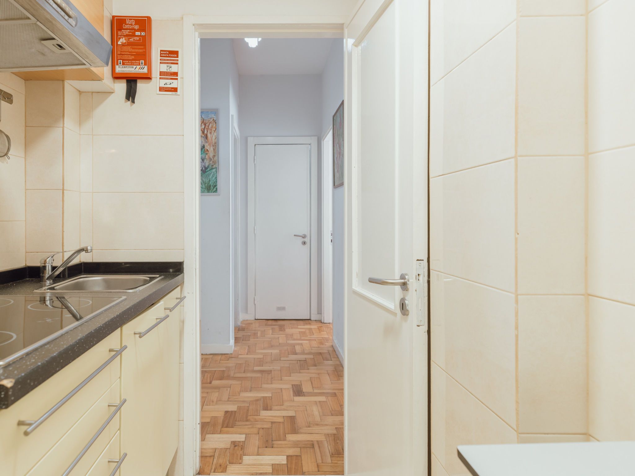 A kitchen with a sink, cabinets, and a herringbone-patterned floor leading to a door.