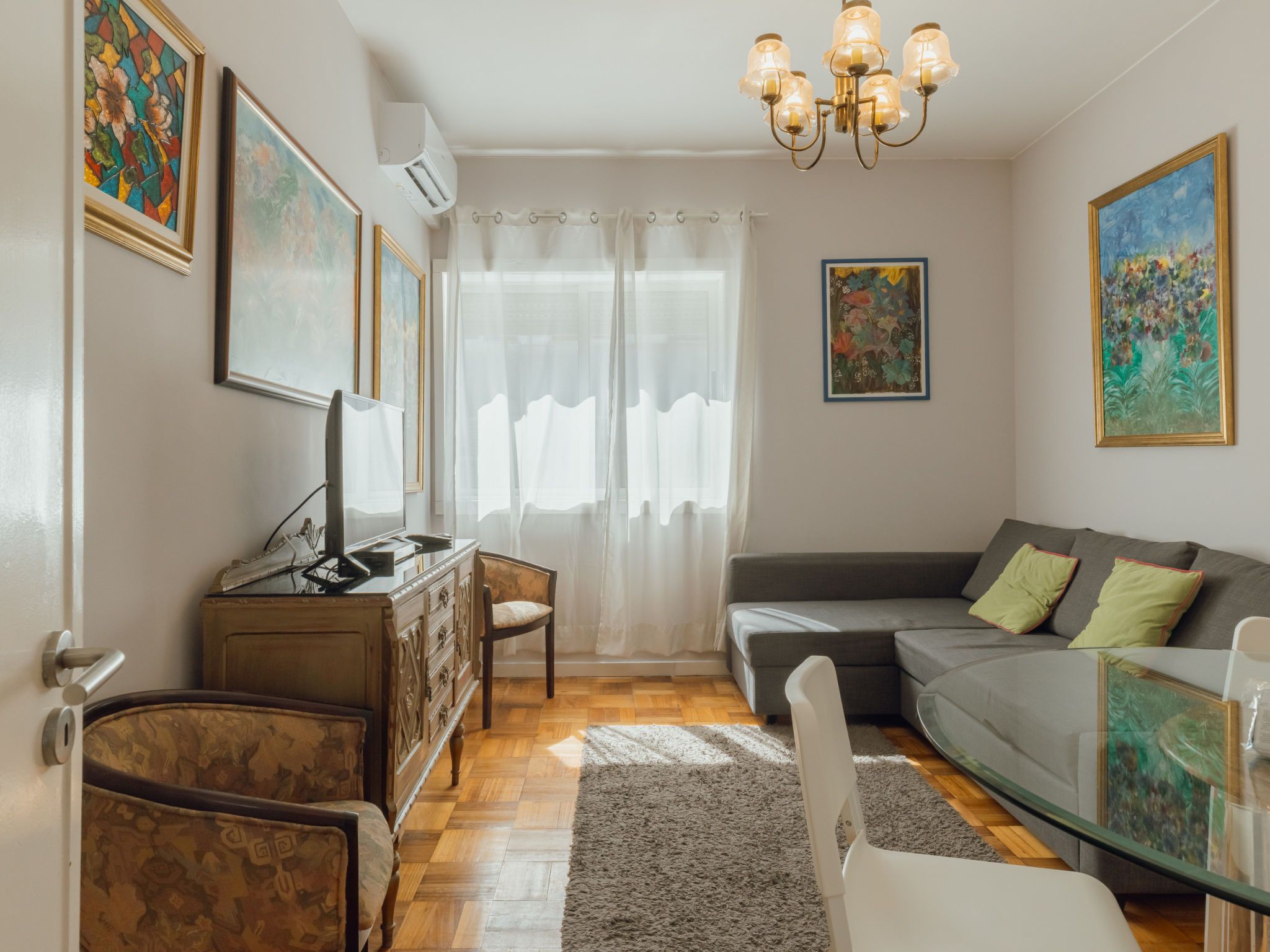 Una sala de estar con un sofá, un televisor sobre un mueble de madera, una araña y obras de arte en las paredes.