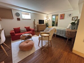 A compact living space with a red sofa, a small round table, a bed with a green bedspread, and a television.