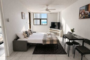 Ein Schlafzimmer mit Bett, Fernseher, Schreibtisch mit Stühlen, einem Fenster mit Ausblick und einem Deckenventilator.