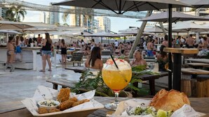 An outdoor dining area with umbrellas, tables, and a view of a busy pool area. - Beachside 1BR Retreat | Ocean Views, Wi-Fi & Pool (Surfers Paradise)
