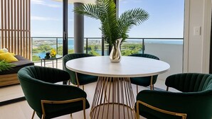 A balcony with a round table and chairs, a potted plant, and a view of the ocean. - Luxury Lakeview 3BR Escape (Robina)