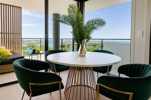 A balcony with a round table and chairs, a potted plant, and a view of the ocean. - Luxury Lakeview 3BR Escape (Robina)