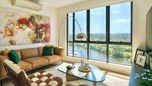 A modern living room with a large window, a brown leather sofa, a glass coffee table, and a painting on the wall. - Luxury Lakeview 3BR Escape (Robina)