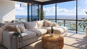 A modern living room with a large sofa, a round wicker coffee table, and a view of a cityscape through large windows. - L54 Sky Ocean View Apt Heated Pool (Surfers Paradise)